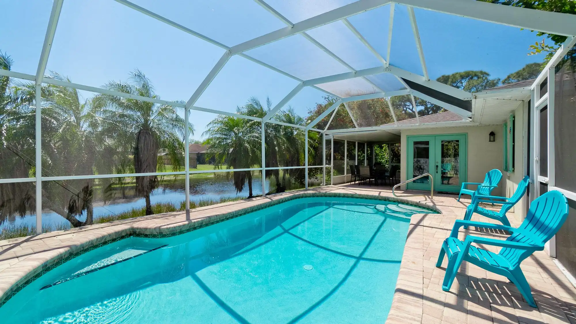 Screened pool looking out over the lake at the pool home at 8403 13th Ave NW in Bradenton, turquoise chairs on the deck